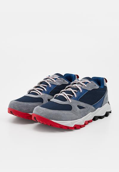 Paire de baskets bleu marine et gris avec semelles crantées rouges et lacets blancs et rouges tachetés sur fond blanc.