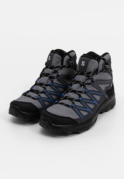 Bottes de randonnée mi-hautes en mesh gris et caoutchouc noir, avec des accents bleus, un capuchon de protection renforcé et un système de laçage sécurisé.