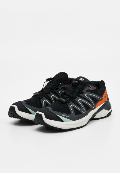 Chaussures de trail running noires et orange avec semelles blanches, matériau Gore-Tex, système de laçage rapide et adhérence texturée pour une utilisation en extérieur.