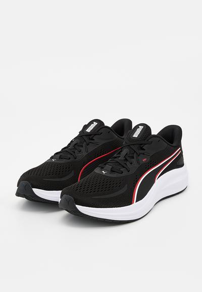 Paire de chaussures de course Puma noires avec semelles blanches, bandes latérales rouges et blanches, et lacets noirs sur fond blanc.