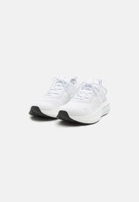 Des chaussures de sport blanches avec une tige en maille texturée, un laçage à l'avant et une semelle en caoutchouc noire. Les accents comprennent des détails gris sur les côtés.