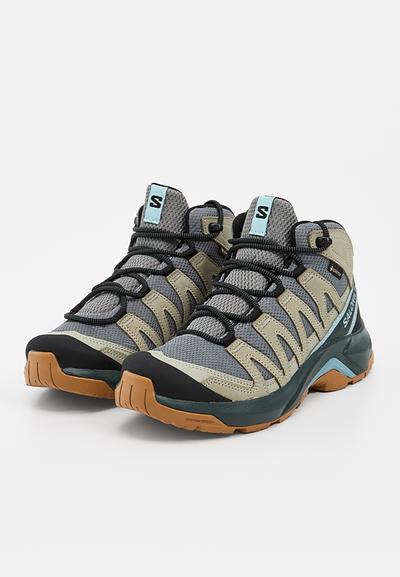 Paire de bottes de randonnée grises et beiges avec lacets noirs, semelles en gomme et accents bleu clair, positionnées côte à côte sur un fond blanc.
