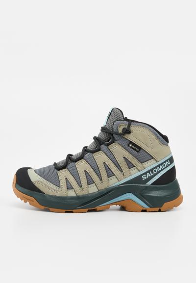 Chaussure de randonnée montante en gris, beige et bleu sarcelle avec des lacets noirs, une semelle en caoutchouc et un logo Salomon sur le côté.