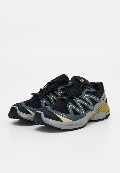 Paire de chaussures de trail de marque Salomon, noires et grises avec des accents jaunes et un système de laçage rapide, placées côte à côte sur un fond blanc.