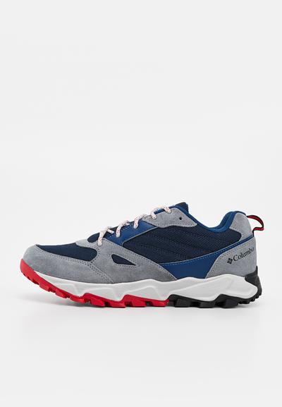 Chaussure de randonnée basse en daim bleu marine et gris avec semelle extérieure rouge et noire, semelle intermédiaire blanche et logo Columbia sur le talon.