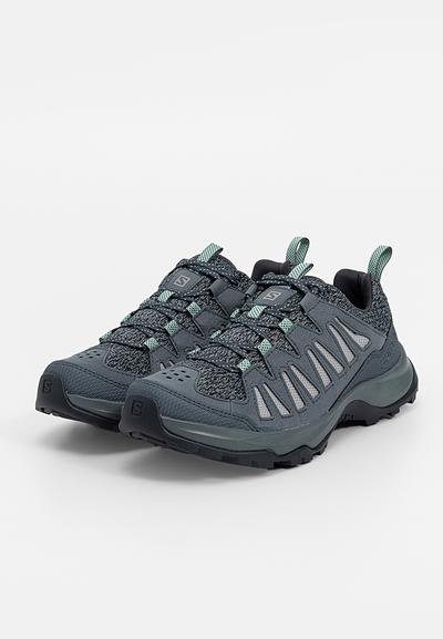 Chaussures de randonnée grises avec un dessus en maille texturée, des accents réfléchissants, une semelle en caoutchouc et des lacets bleu-vert. Conçues pour la durabilité et l'adhérence.