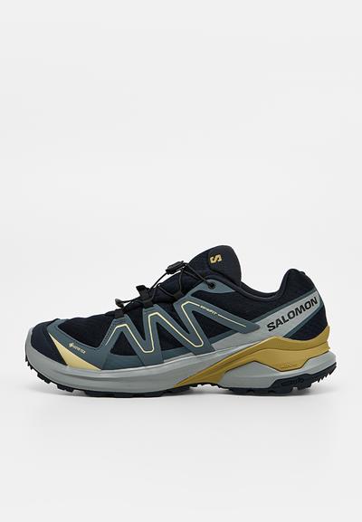 Chaussure de trail running Salomon noire et grise avec des accents jaunes, étiquette Gore-Tex et système de laçage rapide, vue de profil sur fond blanc.