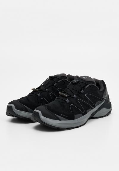 Paire de chaussures de randonnée athlétiques noires et grises avec tissu Gore-Tex et système de laçage rapide, présentées sur fond blanc.