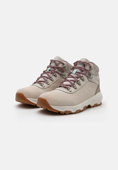 Bottes de randonnée beige clair avec un dessus en suède texturé, des lacets rose et gris, des œillets en métal et une semelle en caoutchouc contrastante.